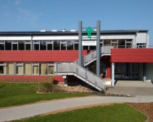 Hochwald Gymnasium, rotes Gebäude mit Treppe, Wiese davor und blauem Himmel